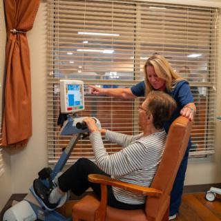 A healthcare professional assists a patient with exercise using a specialized device.