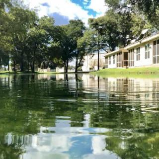 A tranquil view of a lake reflecting the sky and surrounding trees, with a building on the shore.
