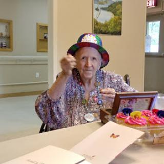 An elderly woman wearing a colorful hat enjoys her time while engaging in crafts.