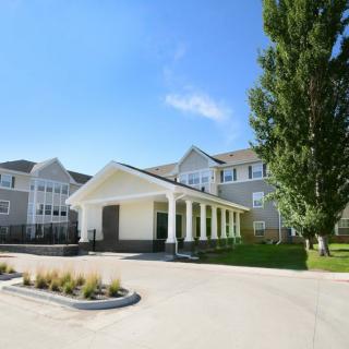 A large residential building with a driveway and landscaped surroundings under a clear blue sky.