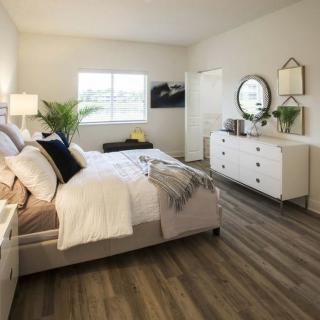 A modern bedroom with a large bed, white dresser, round mirror, and wooden flooring.