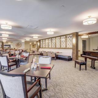 A spacious dining area with neatly arranged tables and chairs, featuring a grand piano in the corner.