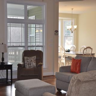 A cozy living room with an armchair, sofa, and a dining area in the background, filled with natural light.