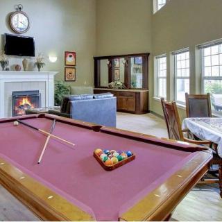 A cozy living room featuring a pool table, fireplace, and large windows.