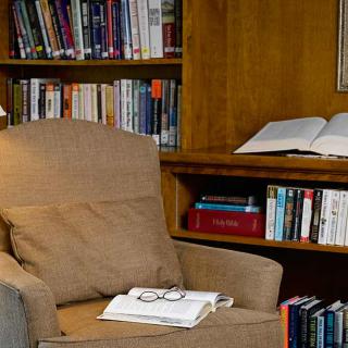 A cozy reading corner with a chair, glasses on a book, and a bookshelf filled with books.