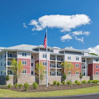 A modern apartment building with a flagpole and landscaped surroundings under a clear blue sky.