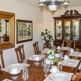 A formal dining room with a long wooden table, elegantly set for a meal, featuring a chandelier and a china cabinet.