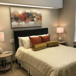 A cozy bedroom with modern decor, featuring a neatly made bed, bedside tables with lamps, and abstract artwork on the wall.