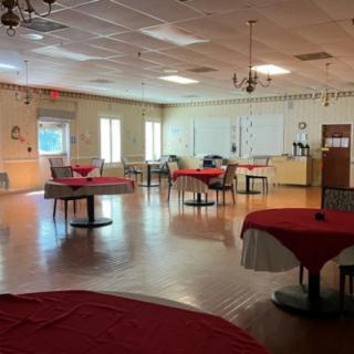 An empty event space with tables covered in red tablecloths and chairs arranged around them.