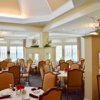 An elegantly decorated dining room with neatly arranged tables and chairs, featuring soft lighting and floral accents.