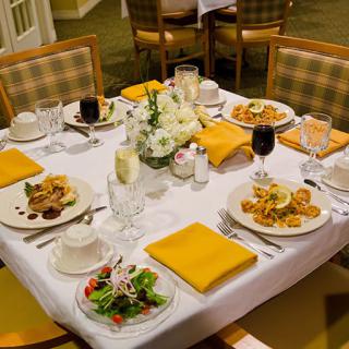 A formally set dining table with plates of food, glasses, and a floral centerpiece.