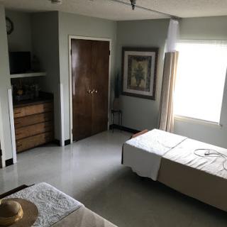 A spacious and minimalist bedroom featuring two beds, a dresser, and natural light from a window.