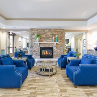 A modern living room with a central fireplace, surrounded by blue chairs creating a cozy seating area.