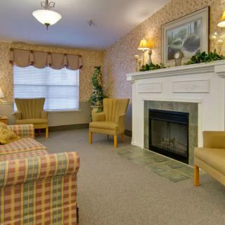 A cozy living room with a fireplace, armchairs, and a plaid sofa, decorated in warm tones.