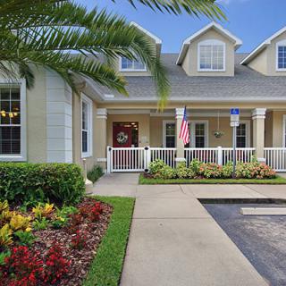 A charming suburban house with a welcoming porch, surrounded by manicured landscaping and displaying an American flag.
