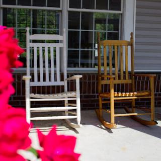Two rocking chairs sit invitingly on a sunny porch, surrounded by vibrant flowers.