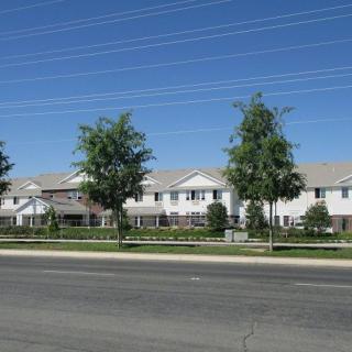 A suburban residential building with trees lining the road under a clear blue sky.
