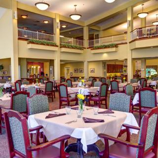 A spacious dining room with neatly arranged tables and chairs, illuminated by chandeliers.