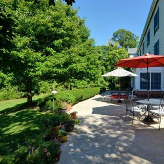 A sunny backyard with a patio featuring outdoor furniture and an umbrella, surrounded by lush greenery and trees.