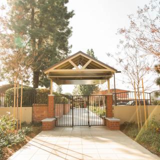 A sunlit pathway leading through a gated entrance, surrounded by trees and greenery.
