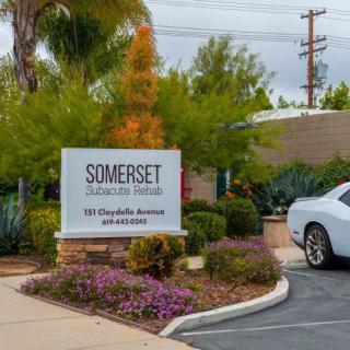 Entrance sign for Somerset apartment homes surrounded by landscaping and adjacent to a parked car.