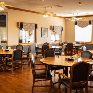 A cozy dining area with round tables and cushioned chairs, featuring large windows and elegant decor.