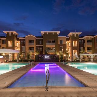 A luxurious apartment complex illuminated at night, featuring a central swimming pool with colorful lighting.