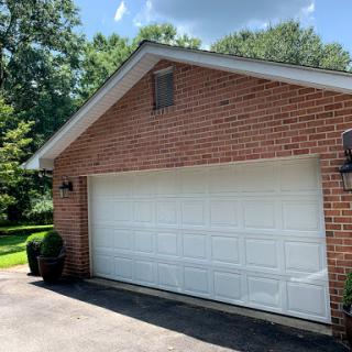 A well-maintained brick garage with a white door, surrounded by greenery.