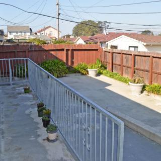 A simple backyard with a patio, potted plants, and wooden fence on a sunny day.