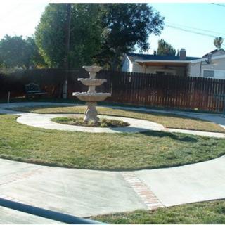 A backyard garden with a central fountain surrounded by a circular pathway.