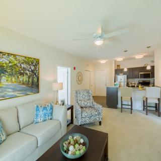 A spacious open-plan living room with modern furnishings and a view into the kitchen area.