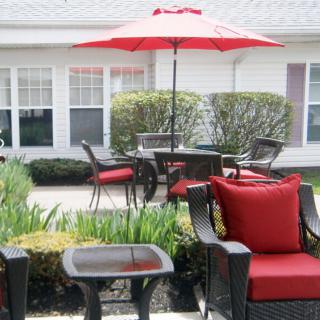 A cozy patio setup with red-cushioned chairs, a table, and a large umbrella in a garden setting.