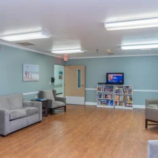 A cozy waiting area with sofas, a television, and a bookshelf in a brightly lit room.