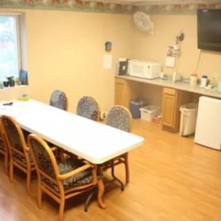 A cozy break room with a long table, chairs, and a kitchenette equipped with a microwave and refrigerator.