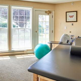 A well-lit exercise room featuring a yoga ball, massage table, and therapy equipment.