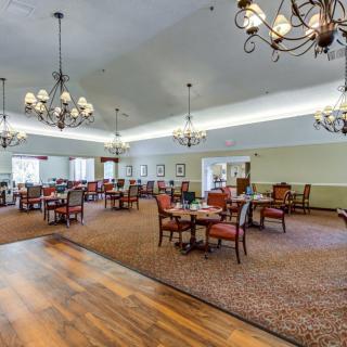 A spacious dining area with elegant chandeliers, tables, and chairs, featuring both carpeted and wood flooring.