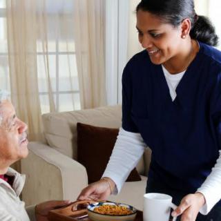 A caregiver assists an elderly person with a meal at home.