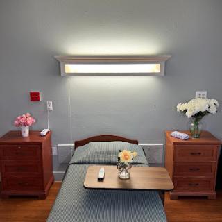 A serene hospital room featuring a single bed, nightstands with flowers, and modern lighting.