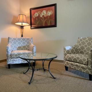 A cozy living room corner with two patterned armchairs, a glass coffee table, and a wall lamp.