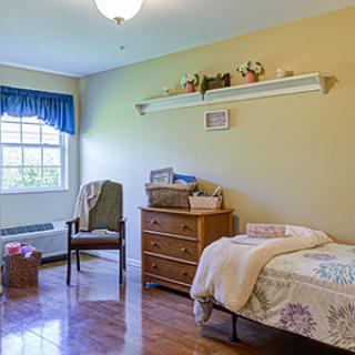 A cozy bedroom featuring a single bed, dresser, and a window with blue curtains.
