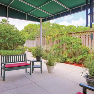 A cozy patio with benches and potted plants under a green awning.