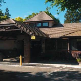 A residential-style building with a sloped roof and a driveway surrounded by trees on a sunny day.