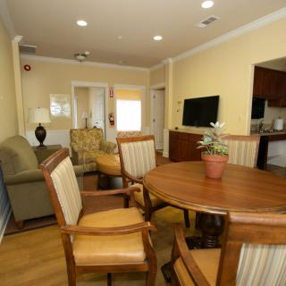 A cozy living and dining area featuring a wooden table, chairs, a sofa, and a TV with an indoor plant on the table.