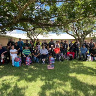 A gathering of individuals enjoying an outdoor community event under the shade of trees.
