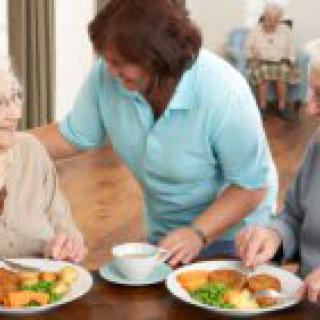 A caregiver assists elderly individuals during a meal at a nursing home.