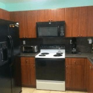 A kitchen with wooden cabinets, a black refrigerator, oven, microwave, and countertop appliances.