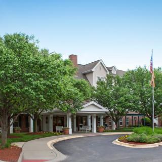 A well-maintained building entrance surrounded by trees with a flagpole and circular driveway.