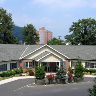 A residential building with a landscaped garden in front, surrounded by trees.