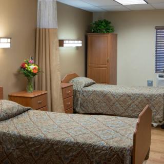A shared hospital room with two twin beds and simple wooden furnishings.