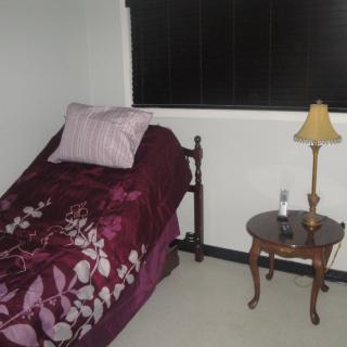 A small bedroom with a single bed, lamp, and nightstand next to a window.